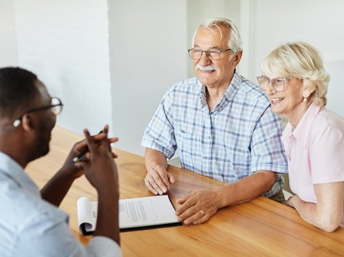 Senior couple with eyeglasses seated across from advisor at table with document